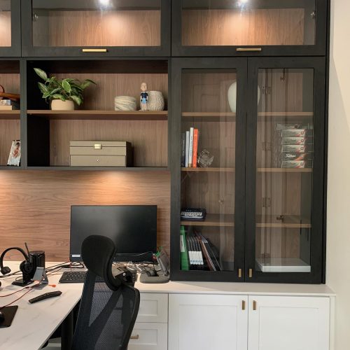 Premium home office with puck lights in the dark wood cabinets and white desk space.